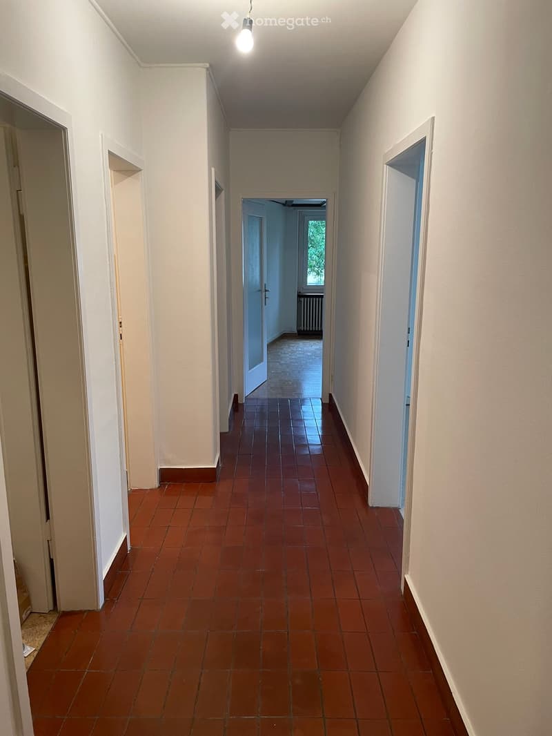 Empty hallway with red tiled floor, white walls, and several open doors leading to other rooms.