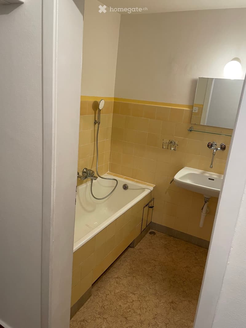 Small bathroom with a bathtub, sink, mirror, and showerhead. Yellow tiles on the walls and a light-colored floor.