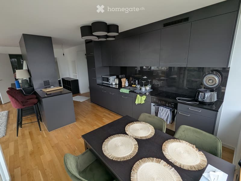 Modern kitchen with dark grey cabinets, a central island, and a dining area. Includes a microwave, oven, fridge, sink, and various kitchen items.