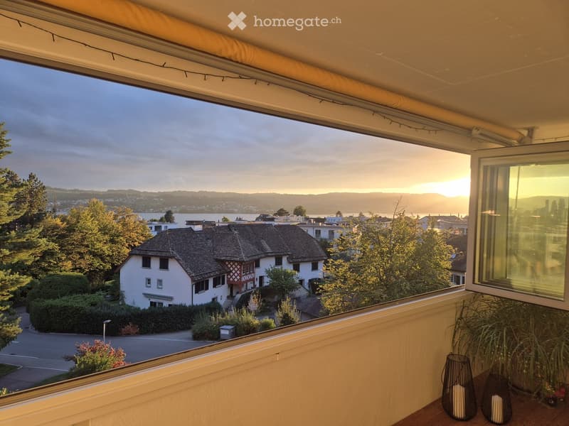 Balcony with a scenic view of a town and lake at sunset, featuring a candle holder and a small plant.