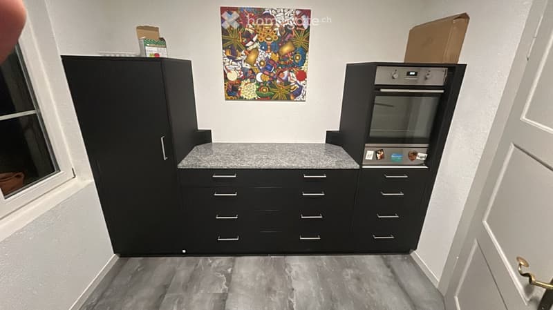 Modern kitchen with black cabinets, a grey countertop, and a built-in oven. A colorful abstract painting hangs on the wall.