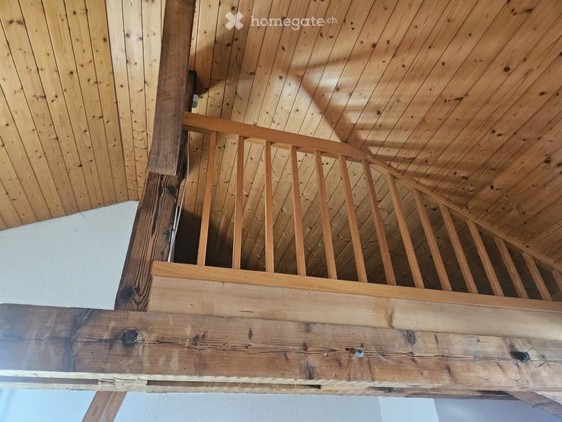 Wooden staircase with a handrail and wooden steps, featuring a slanted wooden ceiling and wooden walls.
