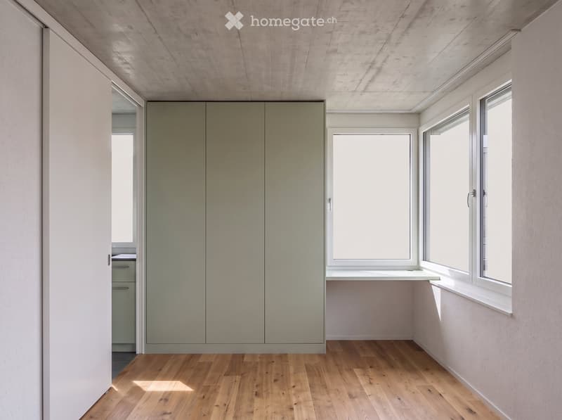 Empty room with light-colored wooden flooring, white walls, large windows, and built-in closet units.