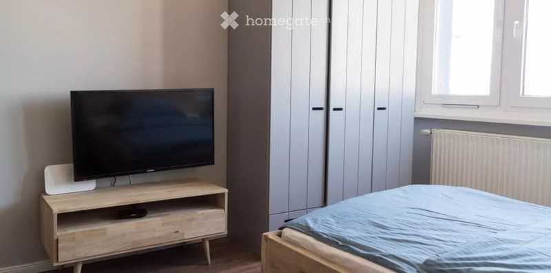 Modern bedroom with a wooden bed, light blue bedding, a flat-screen TV on a wooden stand, and a large wardrobe.