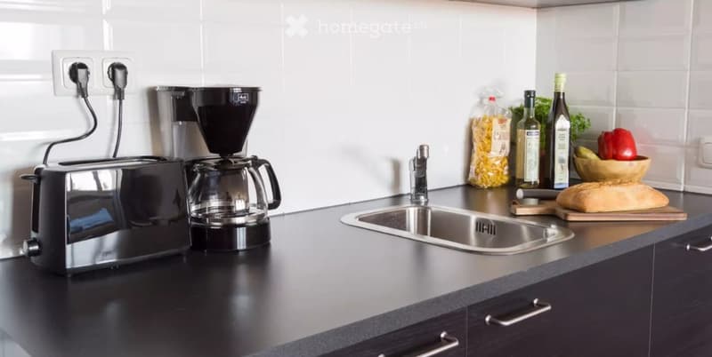 Modern kitchen with black countertops, stainless steel sink, toaster, coffee maker, and various food items on the counter.