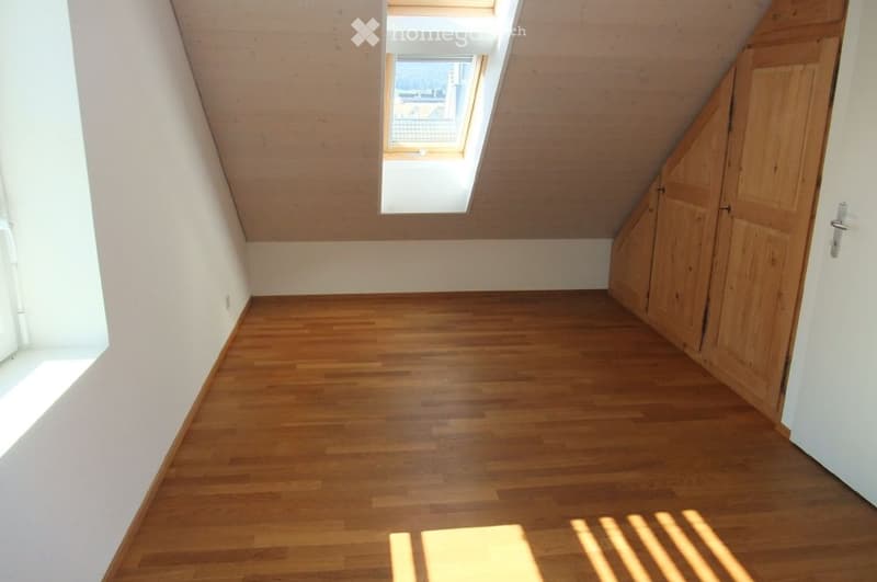 Empty attic room with wooden flooring, white walls, and skylight windows allowing natural light.