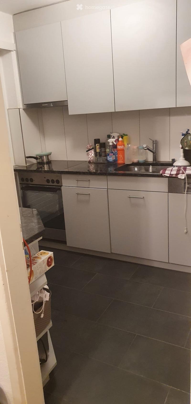 Modern kitchen with white cabinets, dark countertops, and stainless steel appliances. Cleaning supplies are visible on the counter.