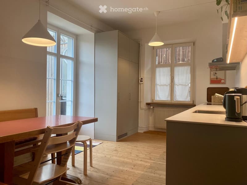 Bright kitchen with wooden flooring, large windows, a dining table with chairs, a kitchen island, and modern appliances.
