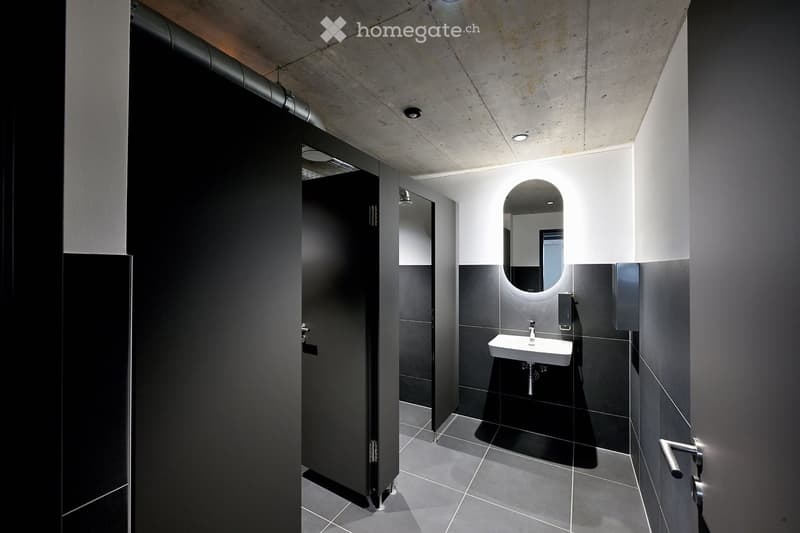 white tiled floor, black tiled walls, a white sink with a silver faucet, a mirror, two urinals with black doors