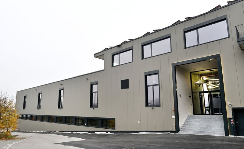 Modern two-story building with a sleek, contemporary design, featuring large windows and a spacious entrance with a staircase leading up to the door.