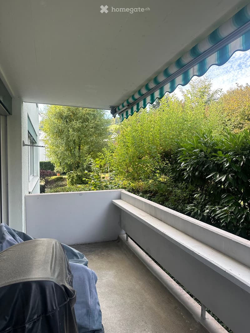 Balcony with a covered awning, white railing, and a view of lush greenery and trees.