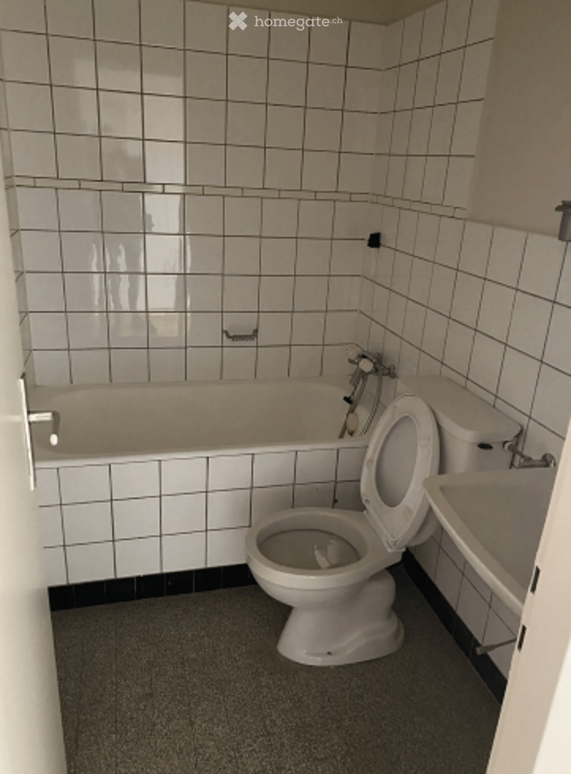 Bathroom with white tiled walls and floor, featuring a bathtub, toilet, and sink.