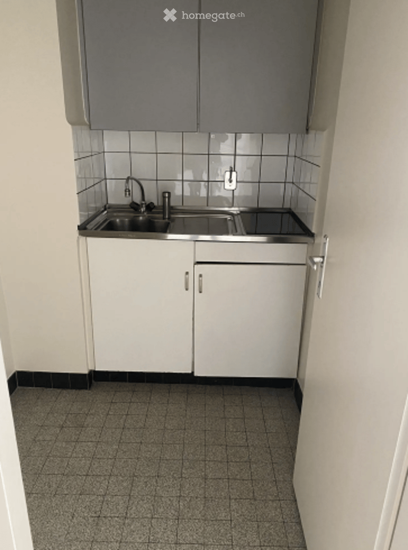 Compact kitchen with white cabinets, stainless steel sink, and tiled walls.