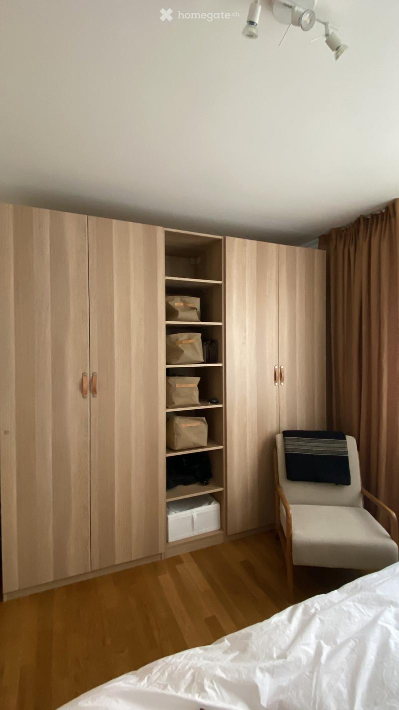 A modern bedroom with a large wardrobe, a single chair, and a bed with white bedding.