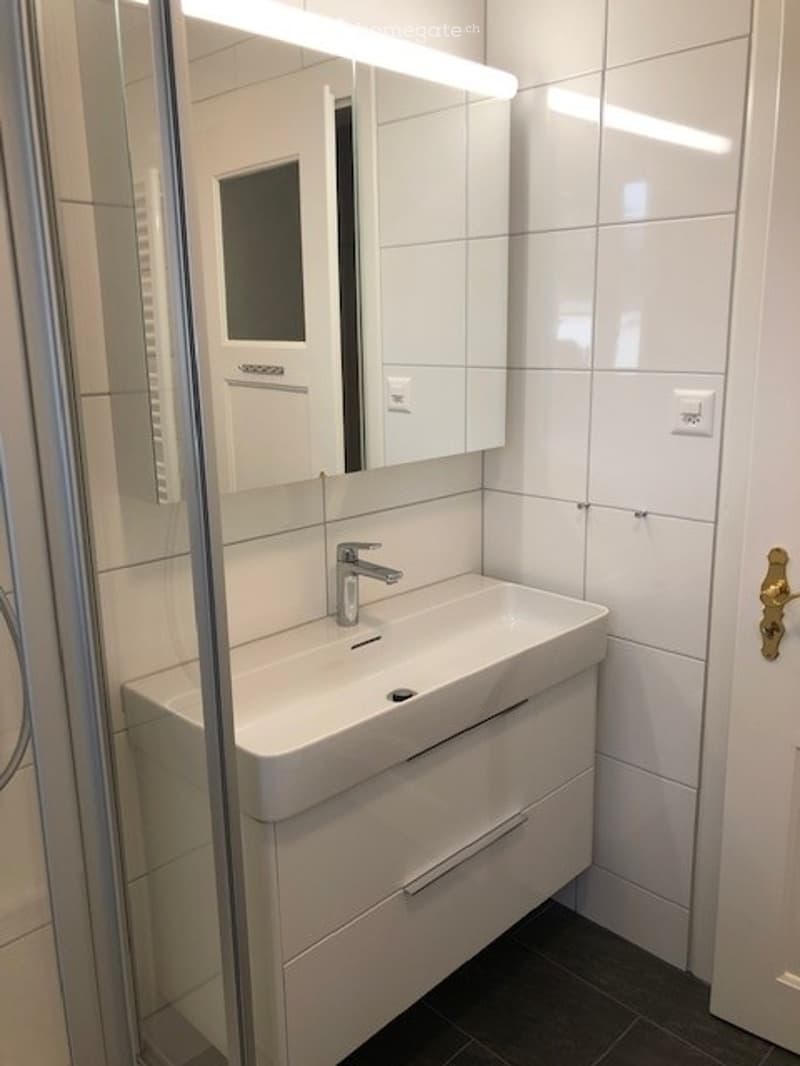 Modern bathroom with white tiles, a white sink with a chrome faucet, a mirrored cabinet, and a sleek design.