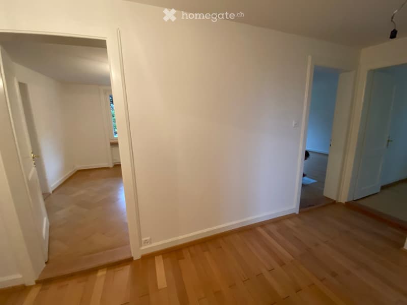 Empty hallway with light wooden flooring and white walls, featuring open doors leading to other rooms.