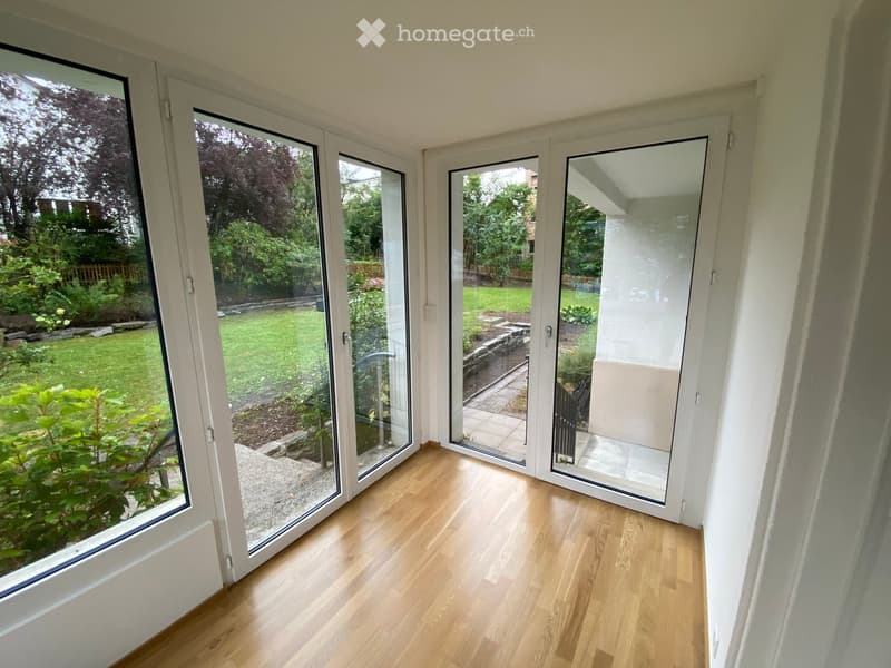 Empty room with light wooden flooring and large glass sliding doors opening to a garden.