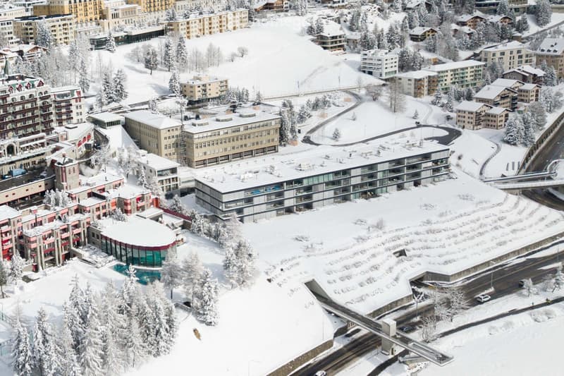 Aerial view of a snow-covered town with multiple buildings, a swimming pool, and surrounding trees.