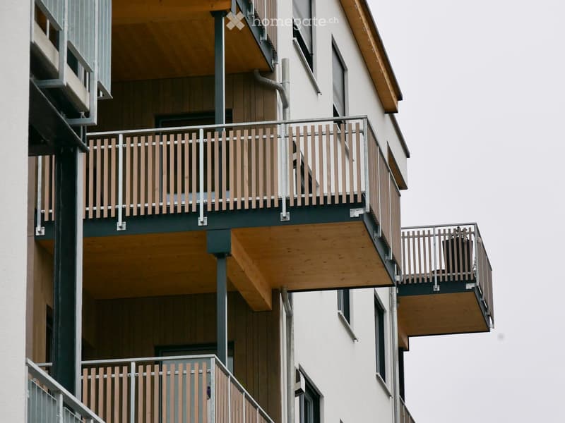 Balconies with wooden railings and metal supports attached to a multi-story building.