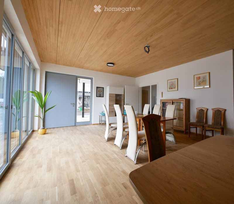 Bright dining area with light wooden flooring, modern dining table and chairs, cabinet, and large windows.