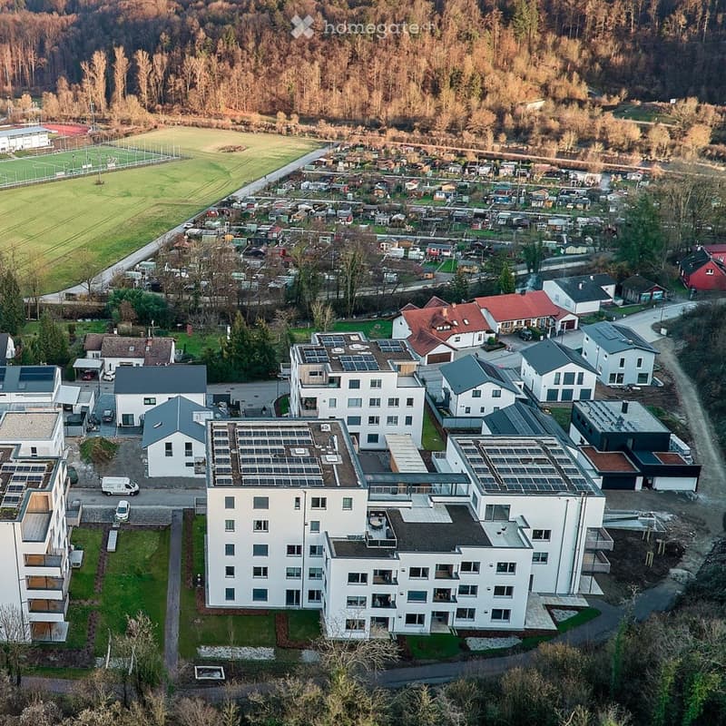 Aerial view of a residential area with multiple modern apartment buildings, surrounded by greenery and a sports field.