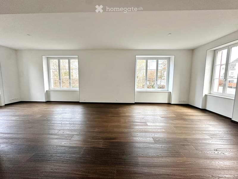 Empty room with wooden flooring and large windows, no furniture or equipment present.