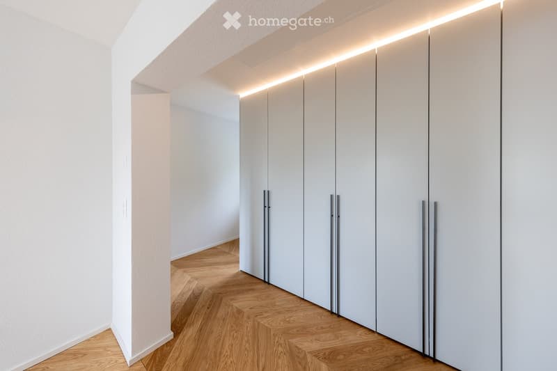 Modern hallway with light wooden flooring, white walls, and built-in white cabinetry with sleek metallic handles.