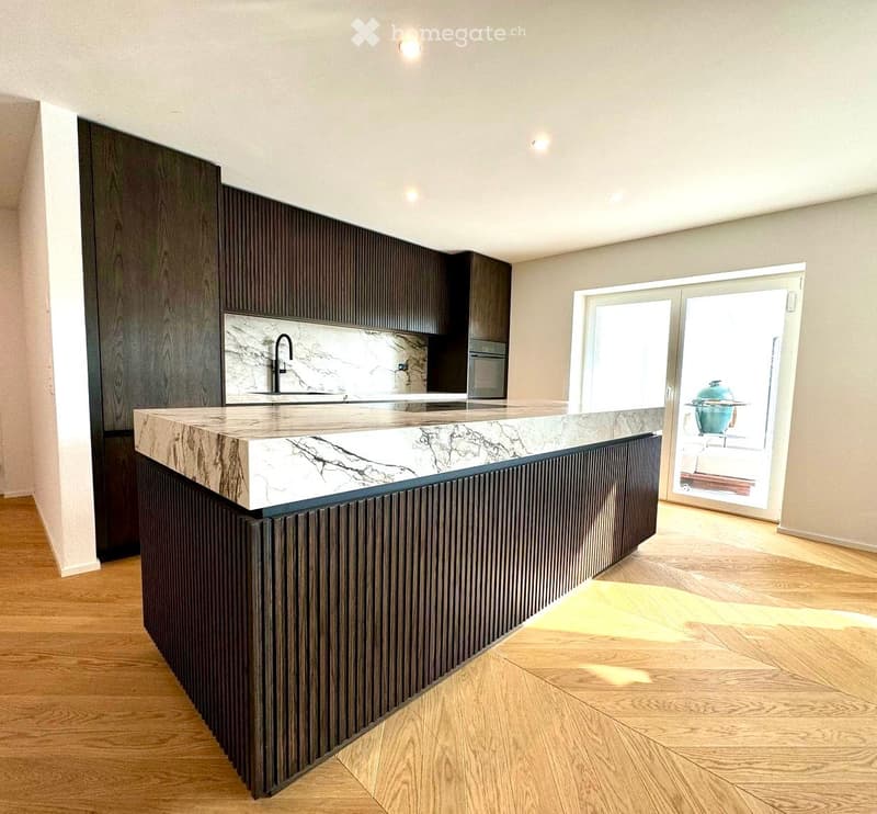Modern kitchen with a marble countertop, dark wooden cabinets, and a sleek sink area. The space features wooden flooring and large windows that allow natural light to fill the room.