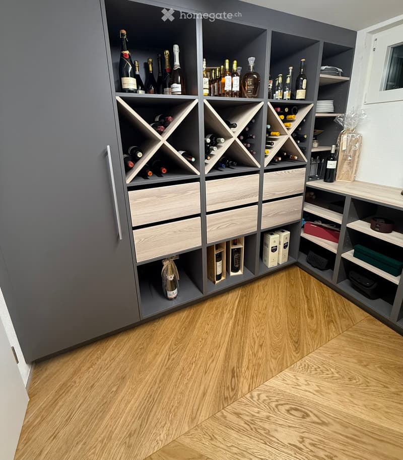 A modern wine storage room with a large wine rack, wooden drawers, and shelves holding various bottles and boxes.