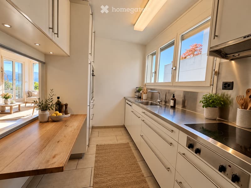 Modern kitchen with white cabinets, stainless steel appliances, and a wooden island. Features include a sink, stove, oven, countertop, and various decorative items.