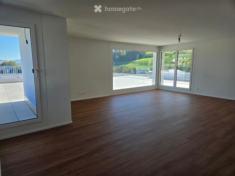 Empty room with wooden flooring, large windows, and sliding glass doors leading to a balcony or terrace area.