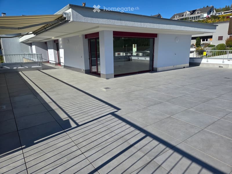 Modern balcony with tiled floor, large sliding glass doors, white walls, and a covered awning.