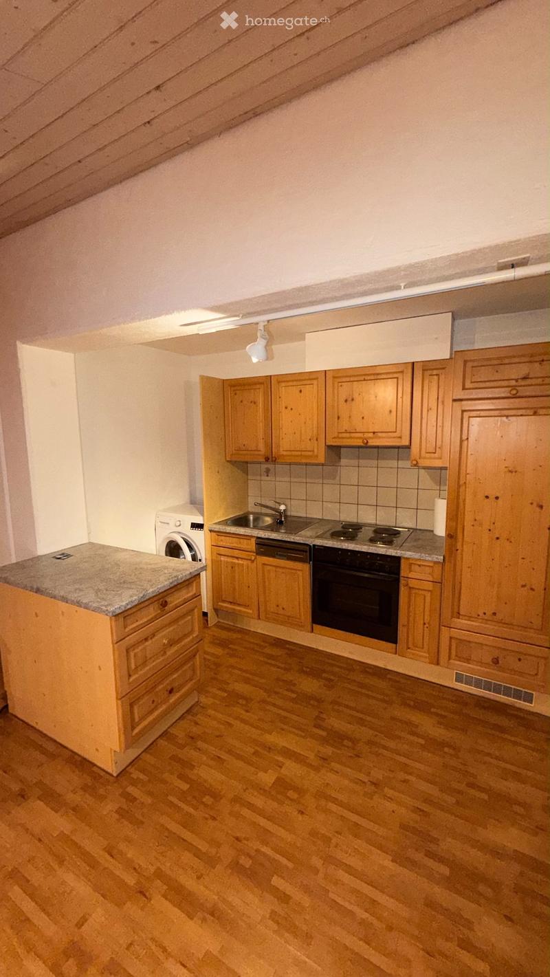 Bright kitchen with wooden cabinets, granite countertop, stainless steel sink, stove, oven, dishwasher, and washing machine. Wooden floor and slanted ceiling.