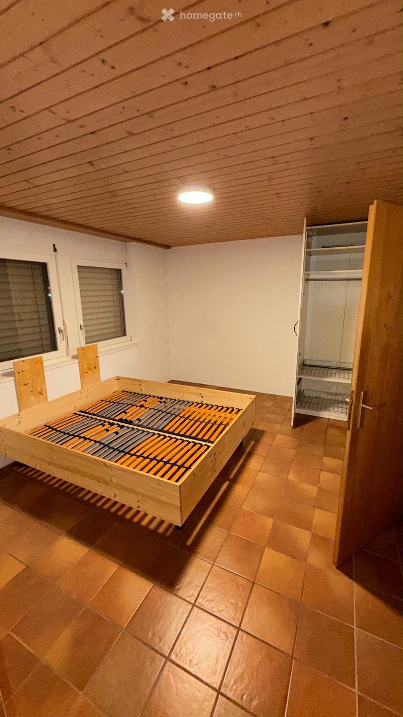 Spacious room with wooden bed frame, built-in wardrobe, tiled floor, and wooden ceiling.