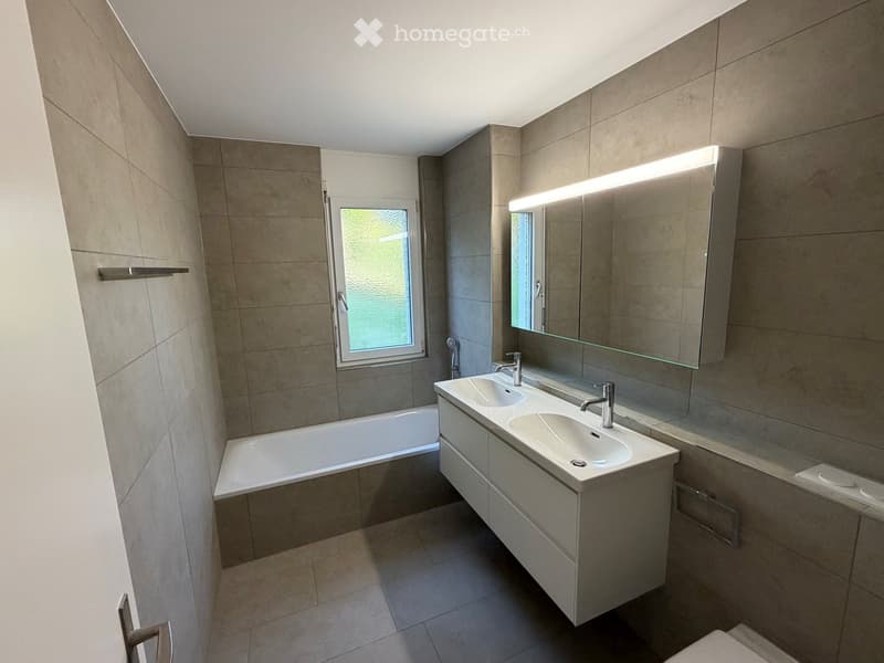 Modern bathroom with a bathtub, double sink, large mirror, and sleek cabinetry.