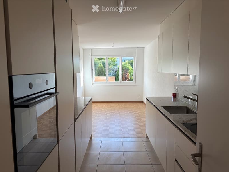 Modern kitchen with white cabinets, granite countertop, and a window overlooking greenery.