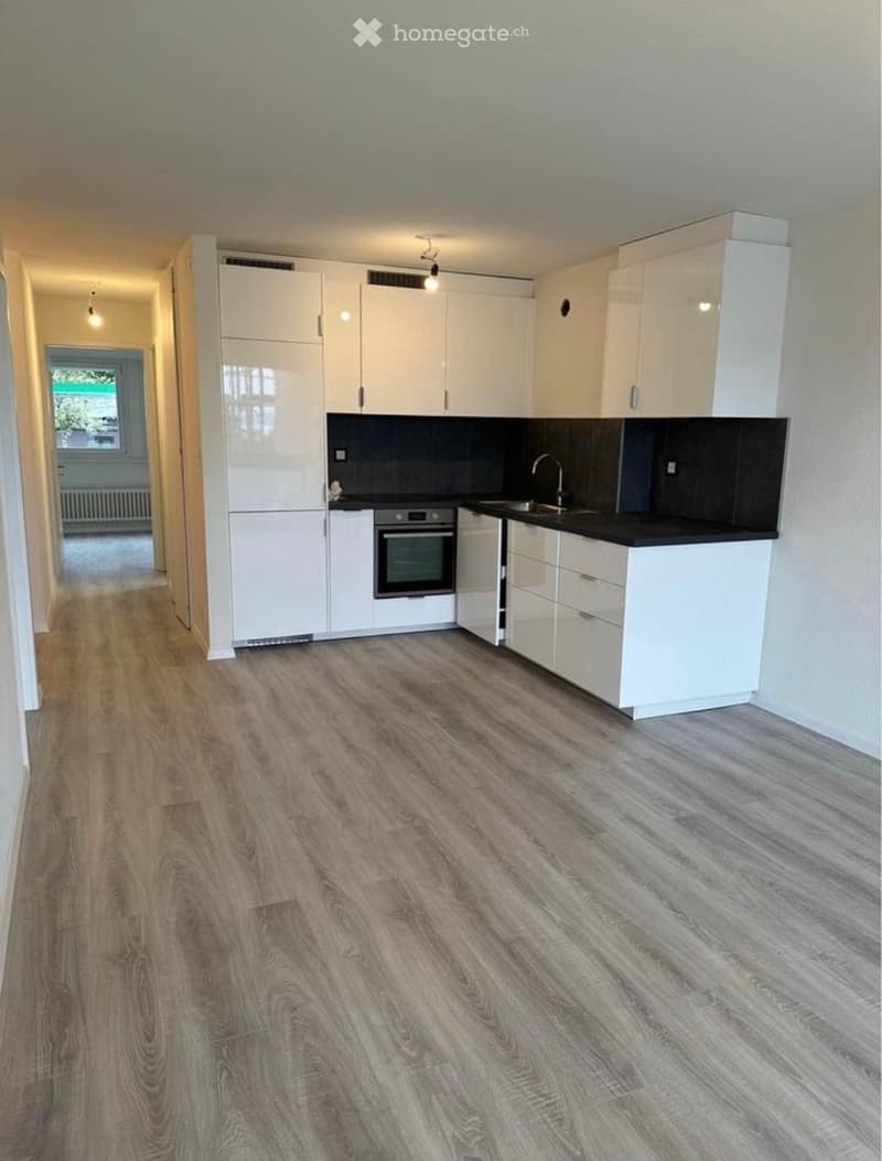 Modern kitchen with white cabinets, black countertops, and a stainless steel oven. Wooden flooring and a window provide natural light.