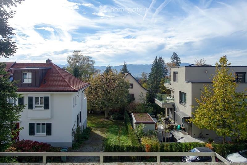 Residential neighborhood with multiple houses, including a two-story house with a red-tiled roof and white walls, surrounded by trees and greenery.