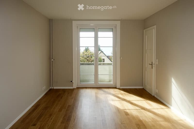 Empty room with wooden flooring, white walls, and a large sliding glass door leading to a balcony.