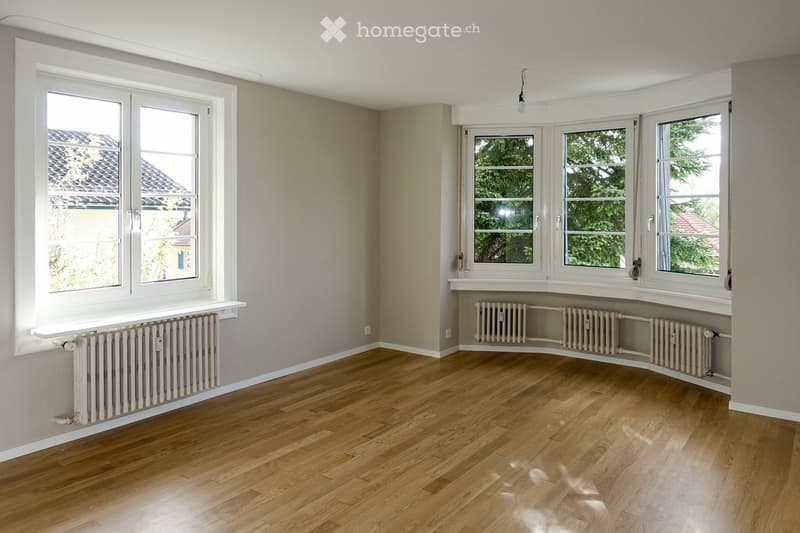 Empty room with wooden flooring, large windows, radiators, and neutral-colored walls.