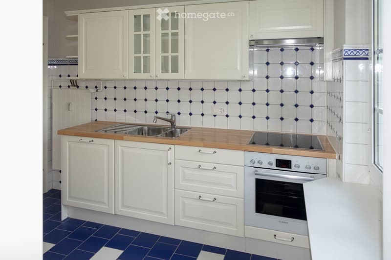 Modern kitchen with white cabinets, wooden countertop, stainless steel sink and faucet, built-in oven, and blue tiled backsplash.