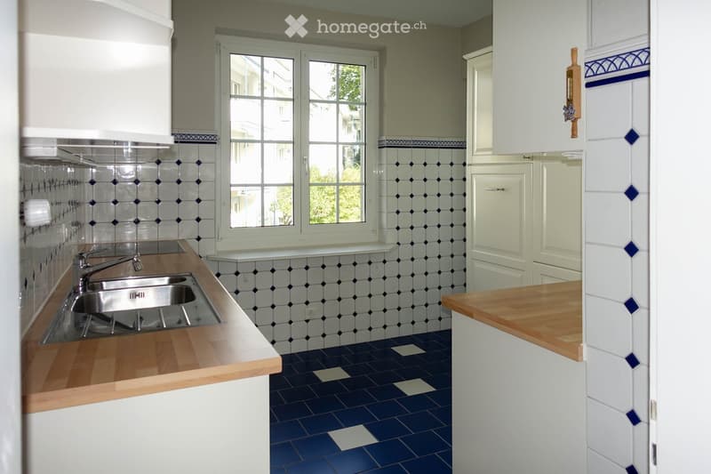 Bright kitchen with white cabinets, wooden countertops, and blue and white tiled walls and floor. Features a double sink with a modern faucet.