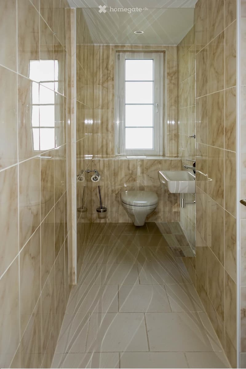 Modern bathroom with beige marble tiles, a toilet, a sink with a chrome faucet, and a toilet paper holder.