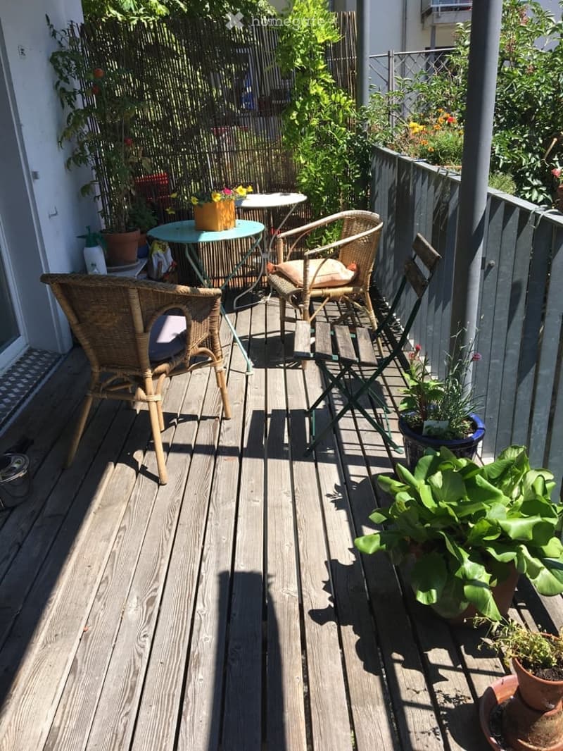 Wooden deck with wicker chairs, small table, and potted plants.