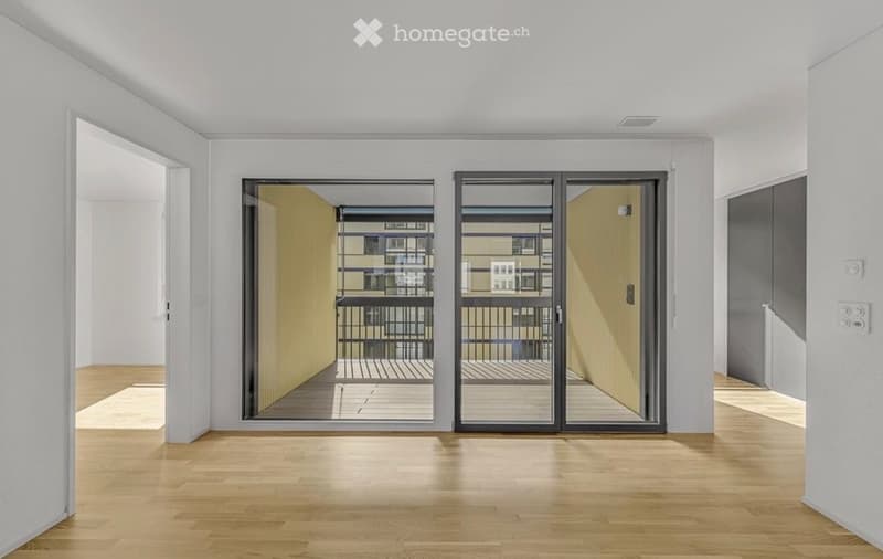 Empty room with light wooden flooring, white walls, and large sliding glass doors leading to a balcony.
