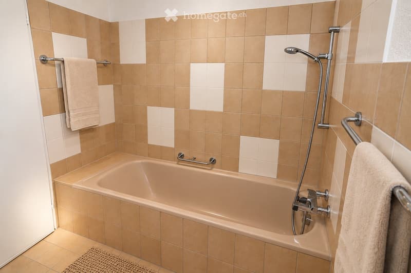 Bathroom with a bathtub, tiled walls, towel rack, and a showerhead.