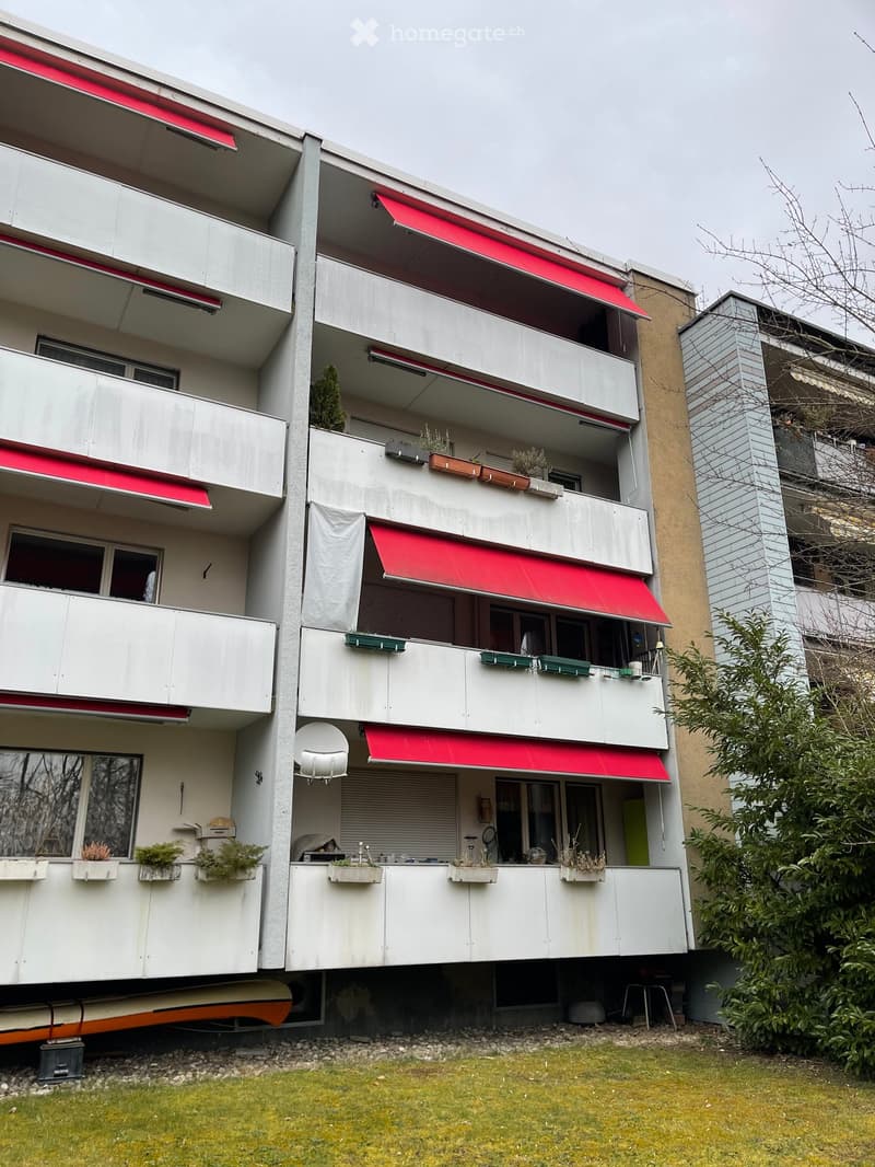 multi-storey building, red awnings, balconies with potted plants, ground-level storage area