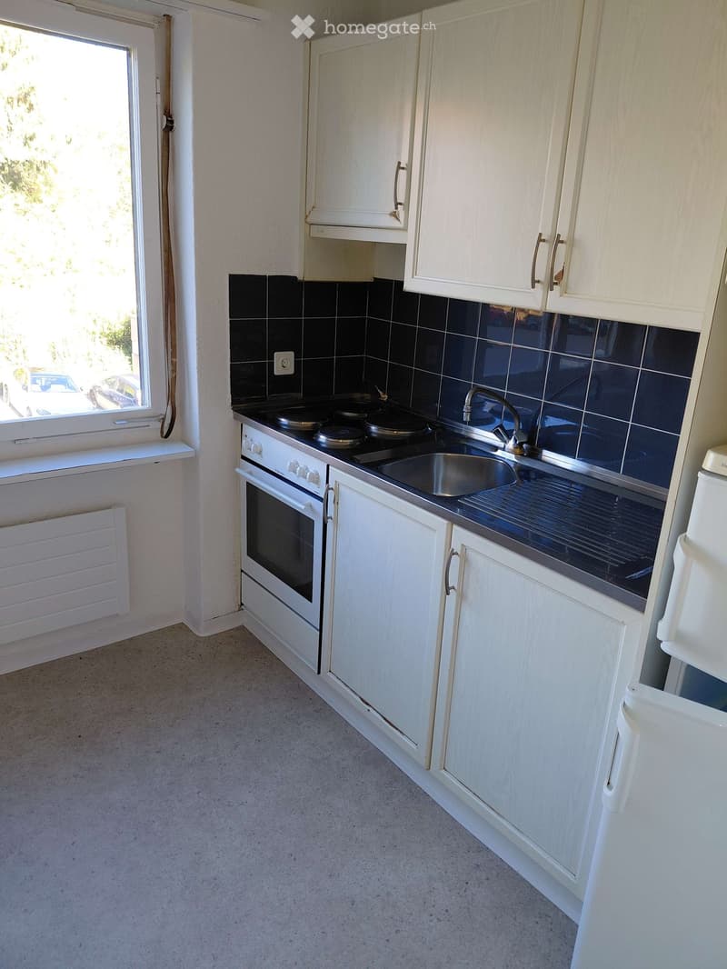Modern kitchen with white cabinets, black tiled backsplash, stainless steel sink, and oven. Features a window with a view of the outside.