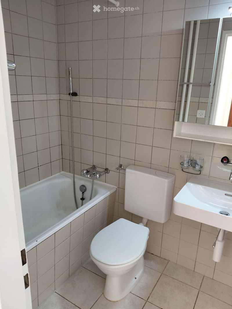 Bathroom with beige tiled walls and floor, featuring a bathtub, toilet, sink, and mirror with two cups on the shelf.