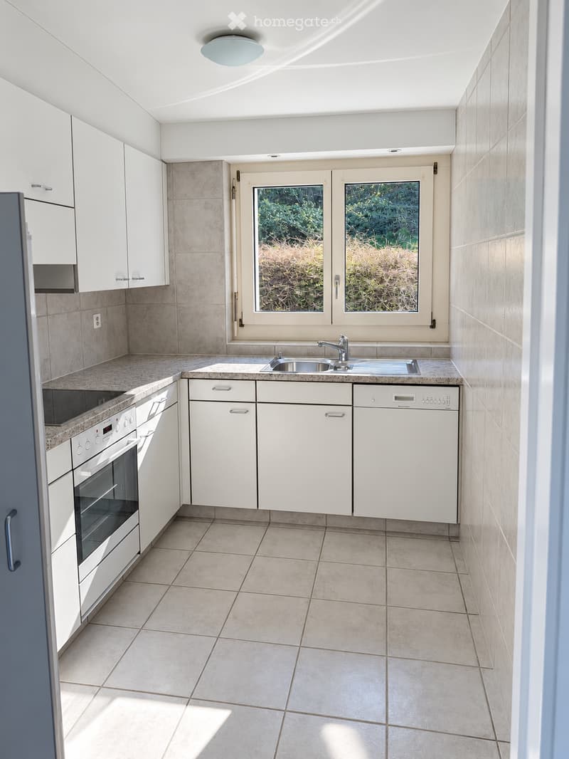 Modern kitchen with white cabinets, stainless steel sink, oven, dishwasher, and tiled flooring.
